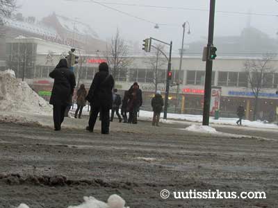 ihmiset laahustavat sohjoisen kadun yli Helsingin Lasipalatsin liepeillä