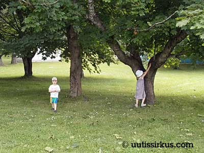 lapset puun alla, tyttö kiipeämäisillään puuhun, poika kävelee poispäin
