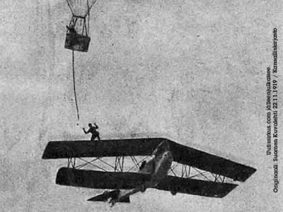 Harry Hill tasapainoilee lentokoneen siivellä ja kurottelee kohti kuumailmapallosta roikkuvaa köyttä