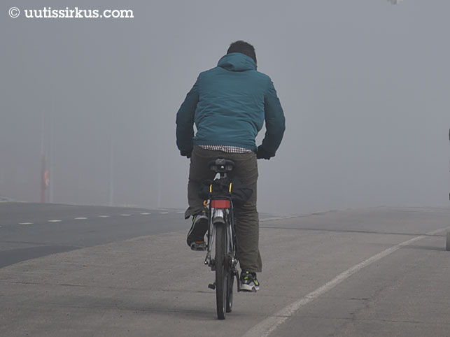 mies pyöräilee sumuisella Lauttasaaren sillalla