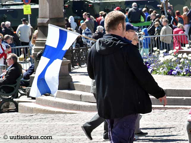 mies kulkee torilla Suomen lippu olallaan, takana väkijoukkoa