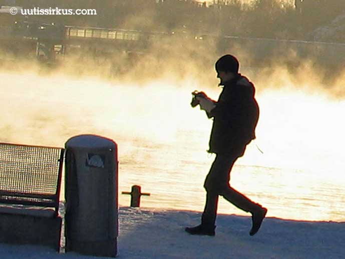 mies kävelee talvisella laiturilla, takana höyryävää vettä