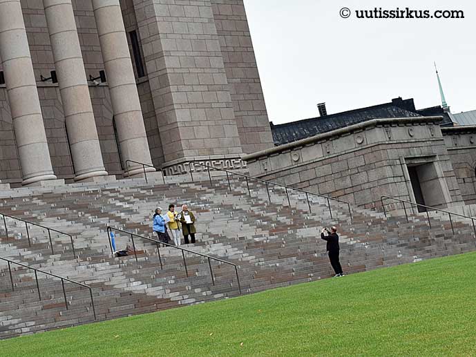 kolme ihmistä seisoo eduskuntatalon portailla, neljäs ottaa heistä valokuvaa