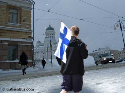 mies kävelee shortseissa Suomen lippu olallaan kohti talvista Senaatintoria