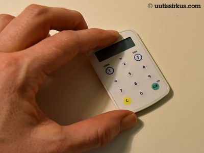 luottokortin kokoinen taskulaskinta muistuttava tunnuslukulaite vasemman käden peukalon ja eyusormen välissä