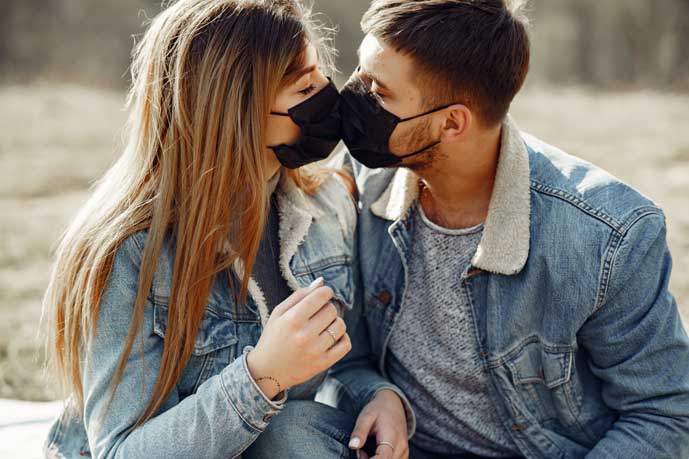 nainen ja mies suutelevat maskit kasvoillaan