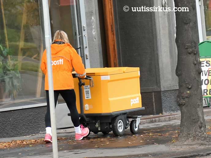 nainen työntää postikärryjä kadulla