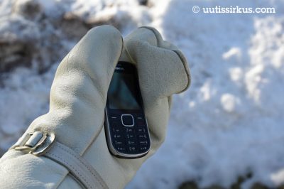 rukkasen verhoamassa kädessä Nokian kännykkä, takana lunta