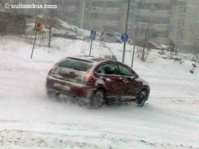 Luminen punainen henkilöauto kiitää lumisella kadulla