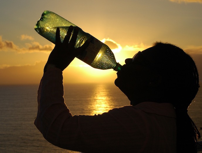 henkilö juo pullosta vettä auringonlaskua vasten