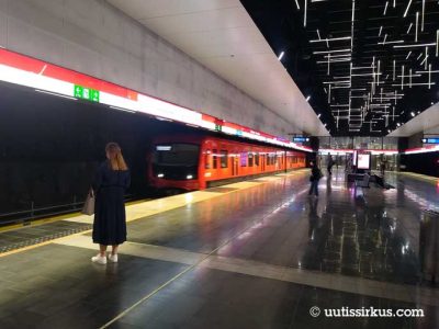 oranssi juna saapuu Keilaniemen metroasemalle, pitkähiuksinen nainen odottaa etualalla