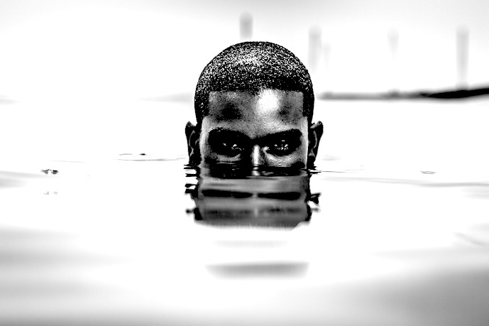 Musta mies nenäänsä myöten vedessä, vain puoli päätä näkyy vedenpinnan yläpuolella