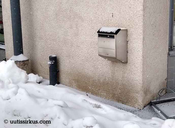 postilaatikko betoniseinässä, lunta kannen päällä ja edustalla