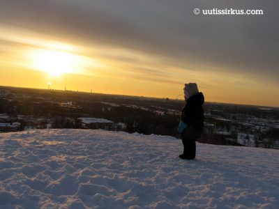 Taapero Malminkartanon täyttömäen päällä talvisen aamuauringon kiivetessä takana näkyvän Helsingin horisontin yläpuolelle.