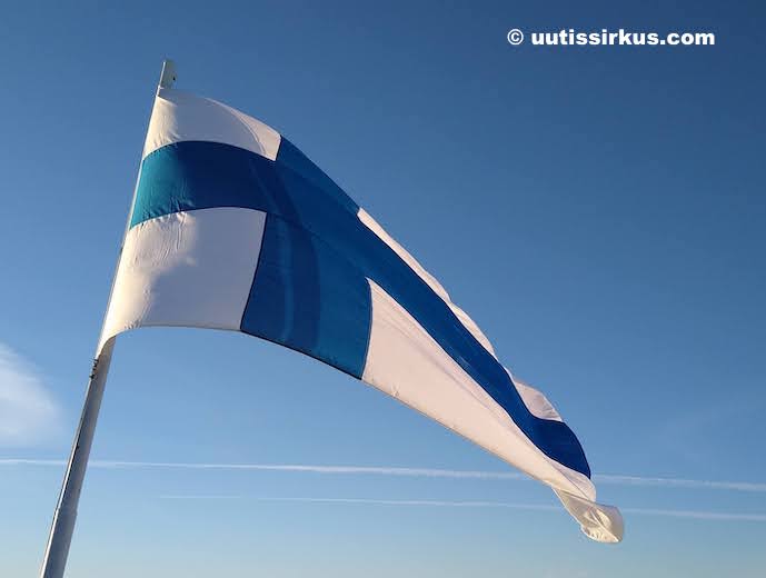 Suomen lippu liehuu sinistä taivasta vasten, läheltä alaviistosta nähtynä