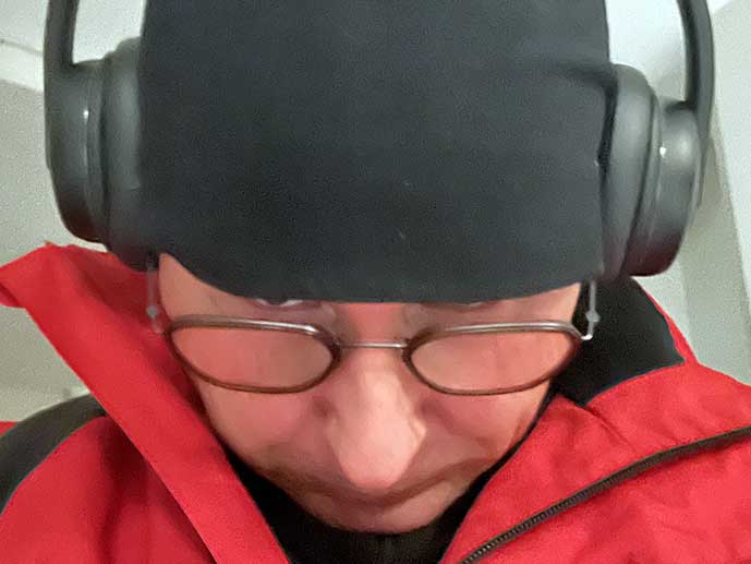 mies punaisessa takissa kaulukset pystyssä, pipo päässä, luurit päässä, katsoo alaspäin