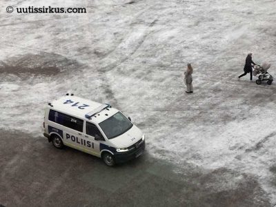 poliisiauto kevyen lumen peittämällä kentällä, yläviistokuva, auton lisäksi näemme yhden paikoillaan seisovan ja yhden lastenvaunuja työntävän ohikulkijan